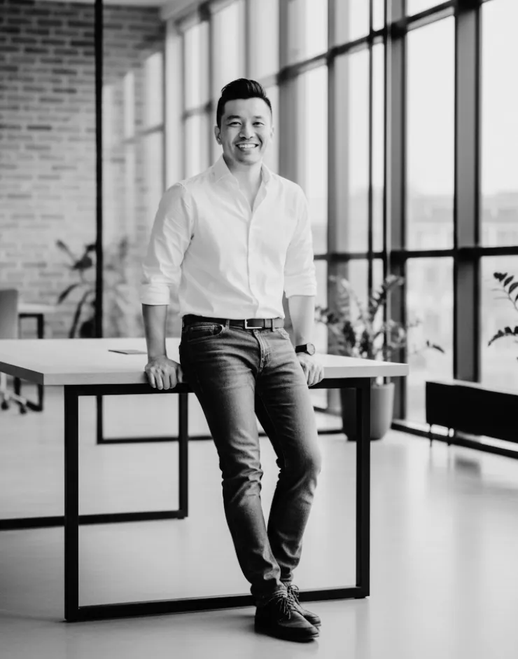Jimmy Banh, Teammember and Lead Designer for Web and UI for FlowMotive Vision, leaning on a table in the office